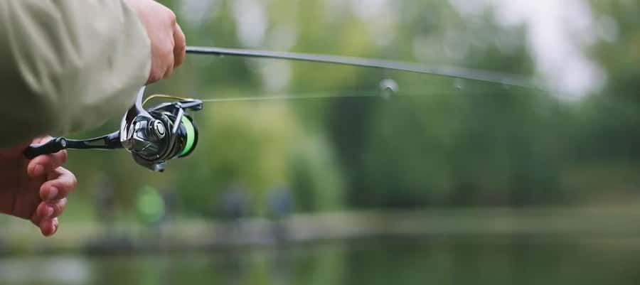 A person holding a fishing rod with a black and green reel over a blurred water background.