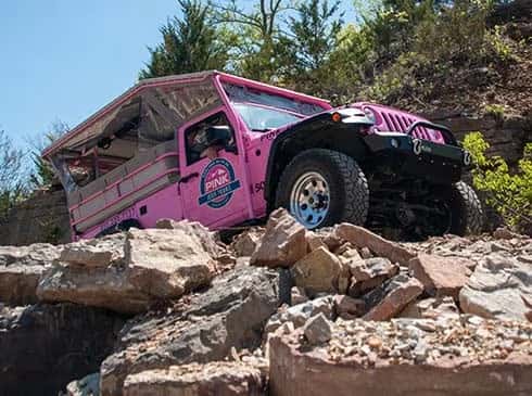 A bright pink Jeep Wrangler navigates rocky terrain during an off-road adventure course.