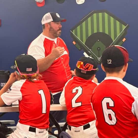 A dad coaching three young players in the dugout
